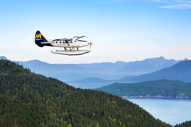 A Harbour Air floatplane flying over forested hills and a coastal inlet