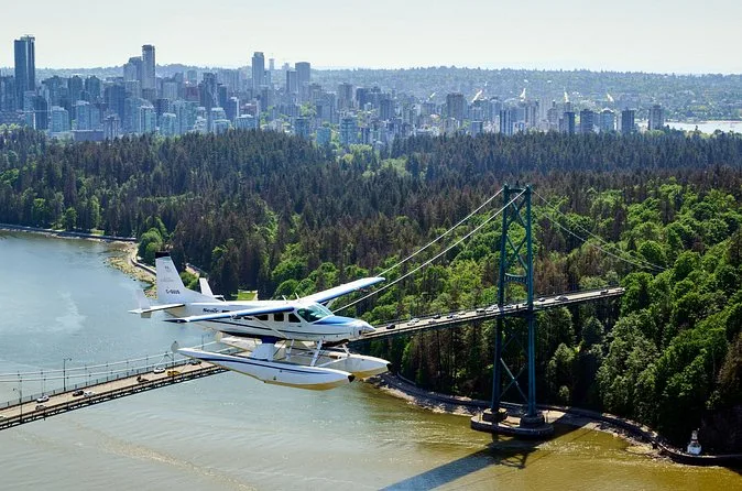 A floatplane flying past the Lions Gate Bridge with Stanley Park and the downtown skyline behind