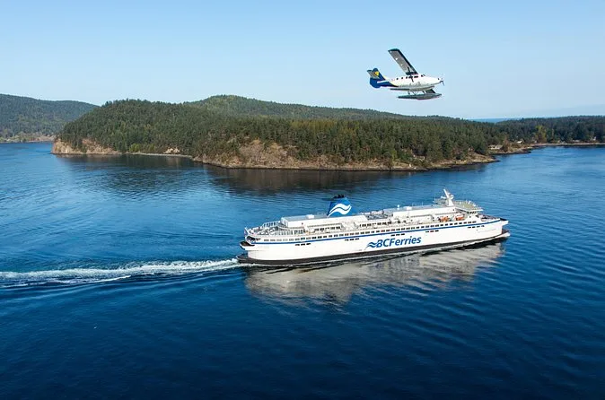 Ein Schiff von BC Ferries fährt über ruhiges Wasser an einer bewaldeten Insel vorbei, darüber ein Wasserflugzeug