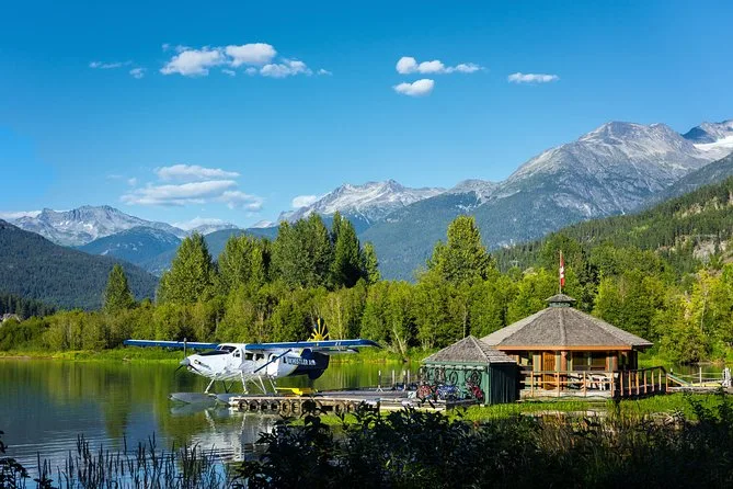 A floatplane moored by a wooden lakeside building with snowy mountains behind