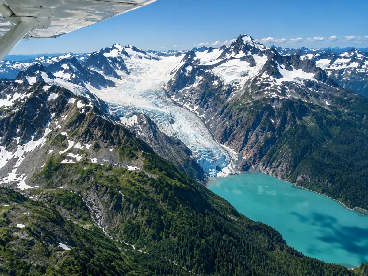 Schneebedeckte Gipfel der Coast Mountains, ein Gletscher und ein türkisfarbener See, gesehen aus einem Wasserflugzeug